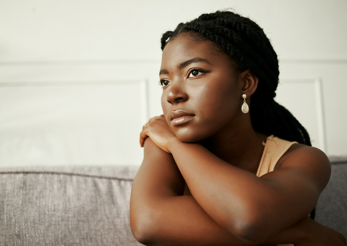 A black women with depression sitting on a couch looking out in the distance