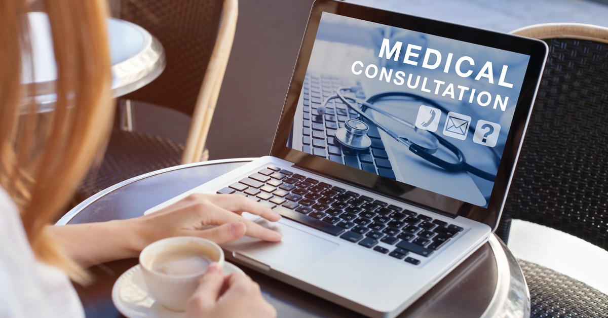 A woman sitting at a table with a cup of coffee and a laptop. The screen of the laptop reads "MEDICAL CONSULTATION."