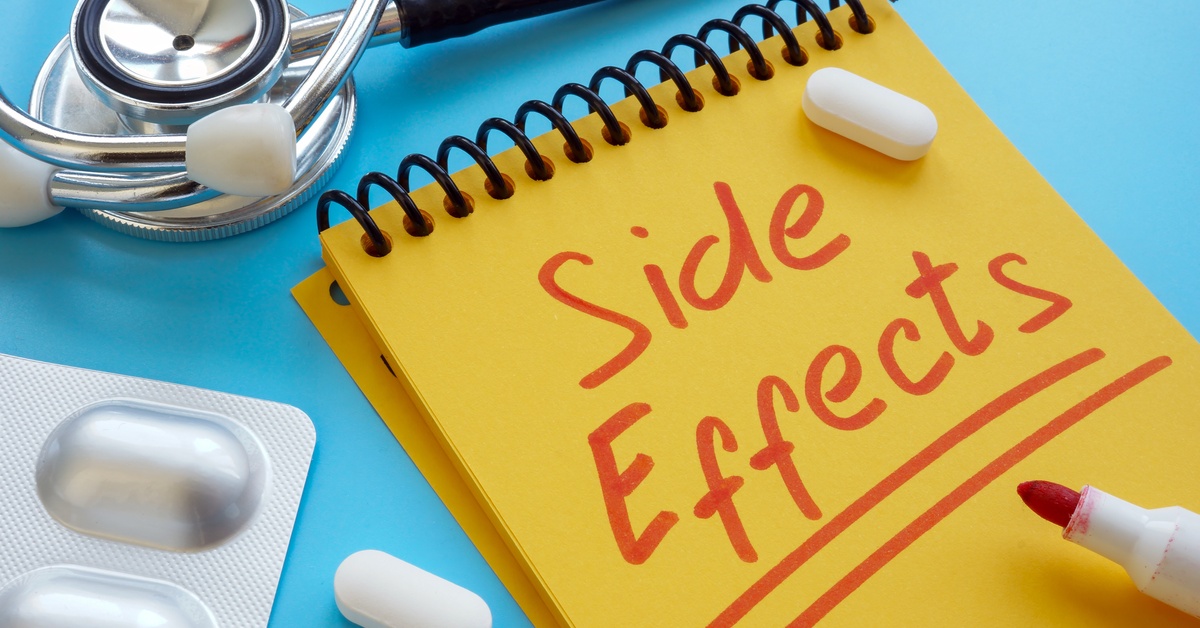 A yellow notepad has the phrase “Side Effects’ written in red letters. White pills and a stethoscope surround the notepad.