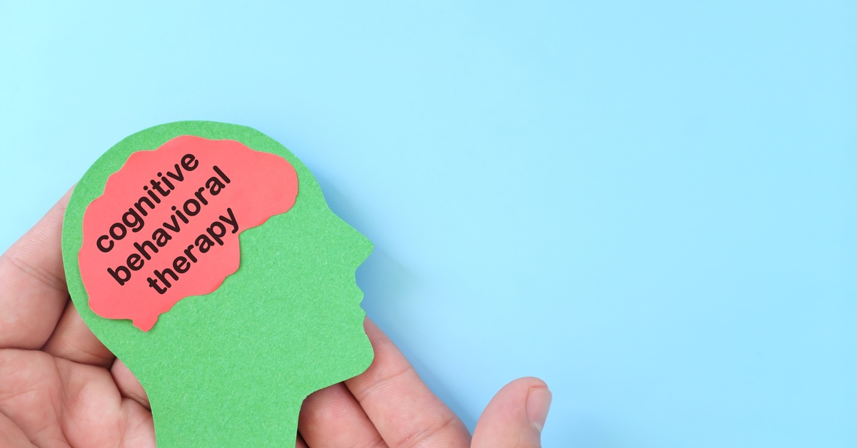 A person holds a green cutout of a human head with a pink brain that says “Cognitive Behavioral Therapy.”