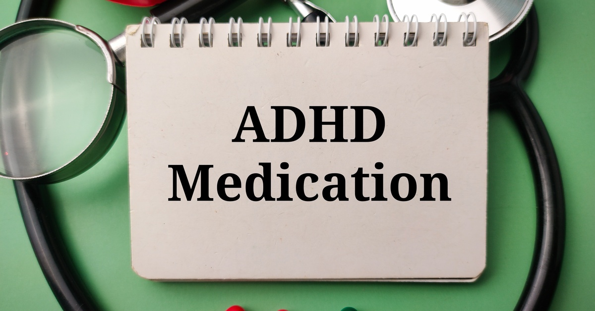 A notebook has the words “ADHD Medication” on the cover. A stethoscope, magnifying glass, and pills surround the notebook.