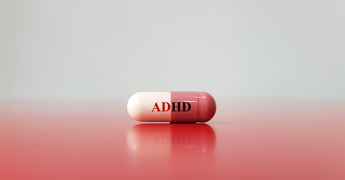 A multi-colored ADHD capsule has the word “ADHD” on the front. The pill sits against a red and white background.