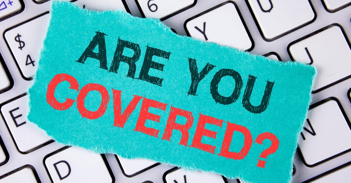 A turquoise paper with bold text 'ARE YOU COVERED?' lies on a computer keyboard, highlighting insurance coverage.