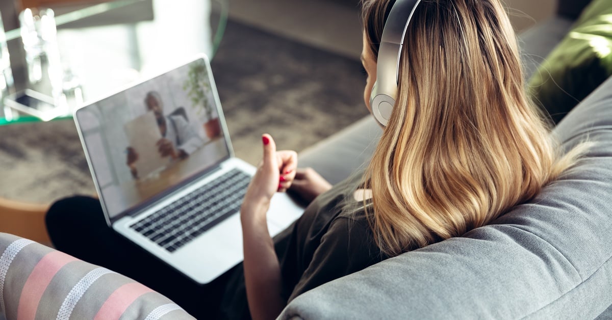 A young person sits in an accent chair with a headset on and a thumbs-up as they speak to an online therapist.