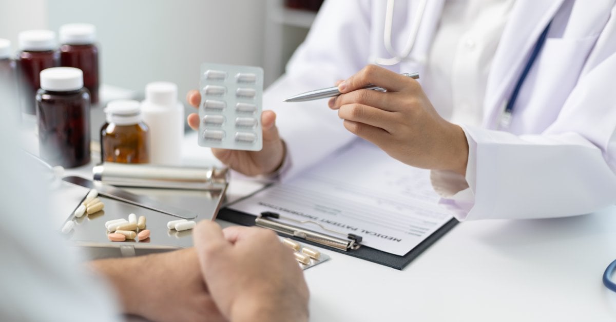 A doctor discusses medication management with a patient, showing a blister pack of pills and explaining dosage instructions.
