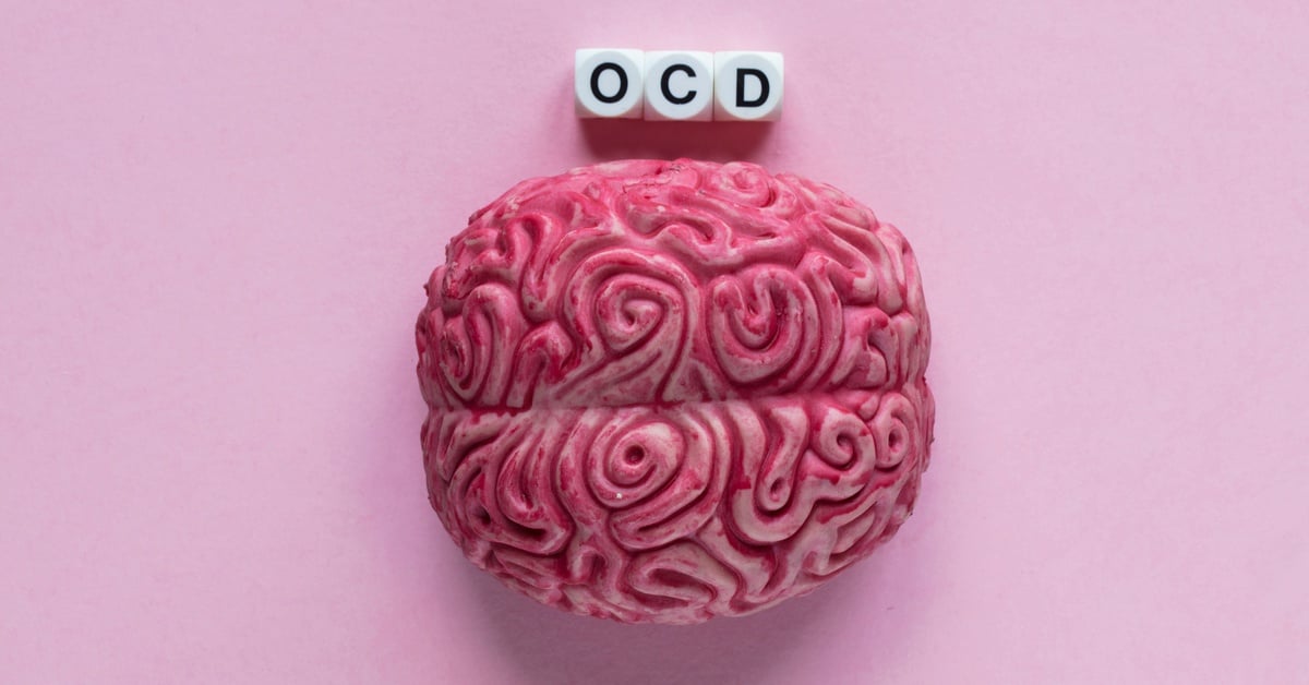 An aerial view of a model of a human brain with white blocks above it with the letters "OCD" on a pink surface.