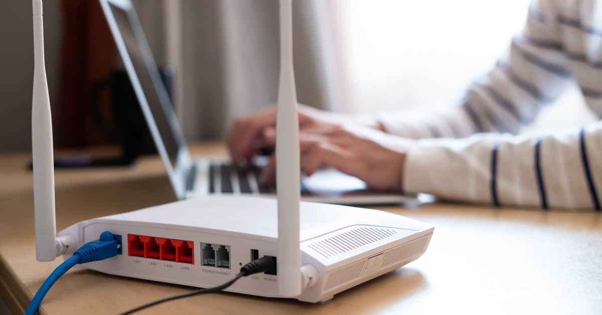 A person uses a laptop for a therapy session with a wireless router in the foreground, ensuring a stable internet connection.