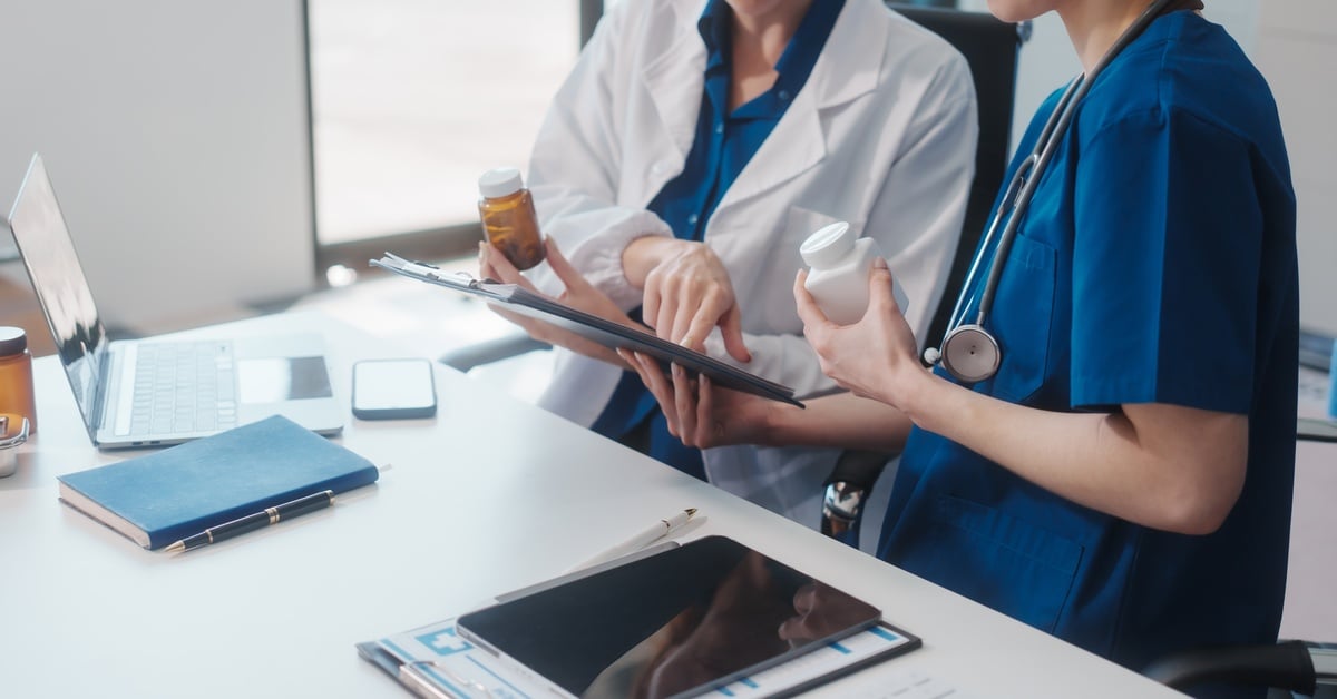 Two healthcare professionals review a medication management plan on a tablet while holding prescription bottles.