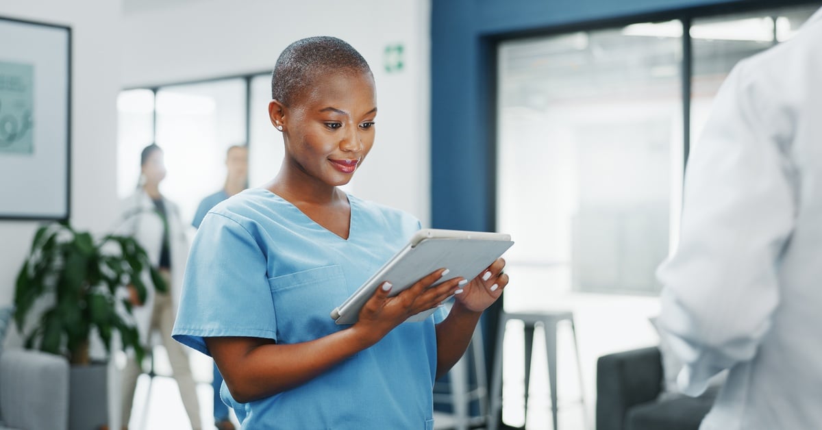 A healthcare provider in blue scrubs reviews patient information on a tablet for medication adjustment and treatment plan.