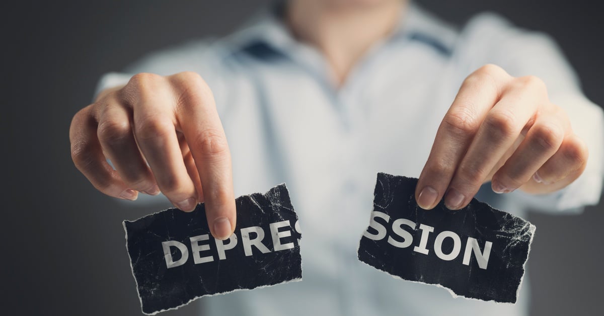 A person in a light shirt tears a black paper labeled “depression," symbolizing emotional struggle and mental health.