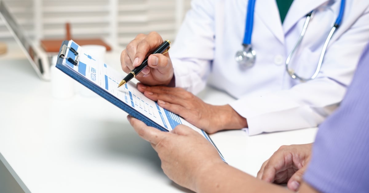 A doctor reviews a medical form with a patient, pointing to chart details during an in-office consultation.