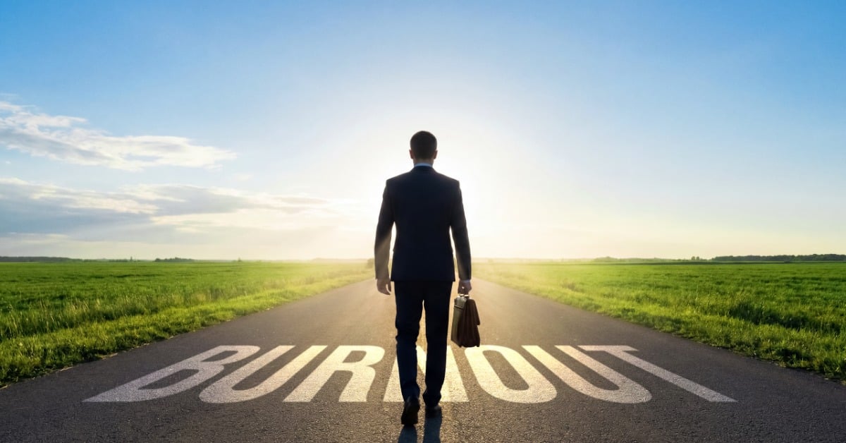 A businessman walks down an open road with the word “Burnout” written on the pavement, symbolizing career stress and exhaustion.