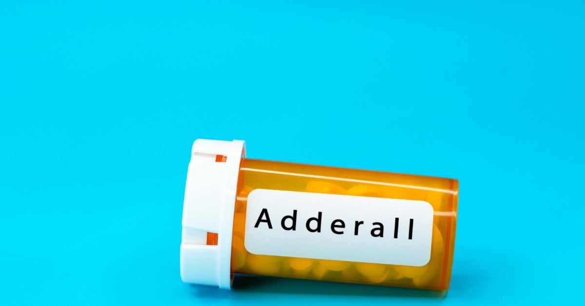 An orange prescription pill bottle with a white label reading Adderall lying on its side against a bright blue background.