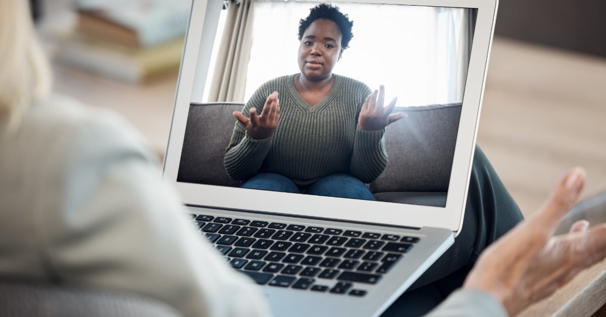 A woman gestures expressively on a laptop screen during a therapy video call with a professional psychiatrist.
