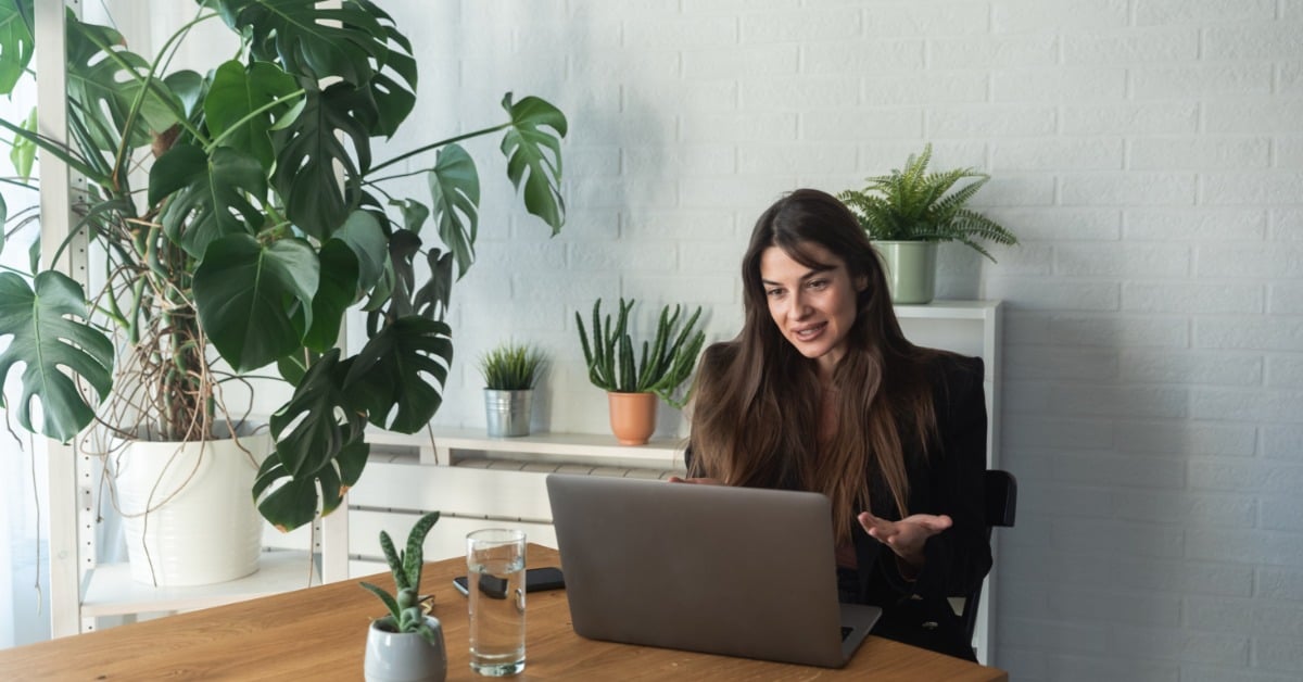 A therapist speaks openly during a telehealth mental health services video call from a calm, plant-filled workspace.