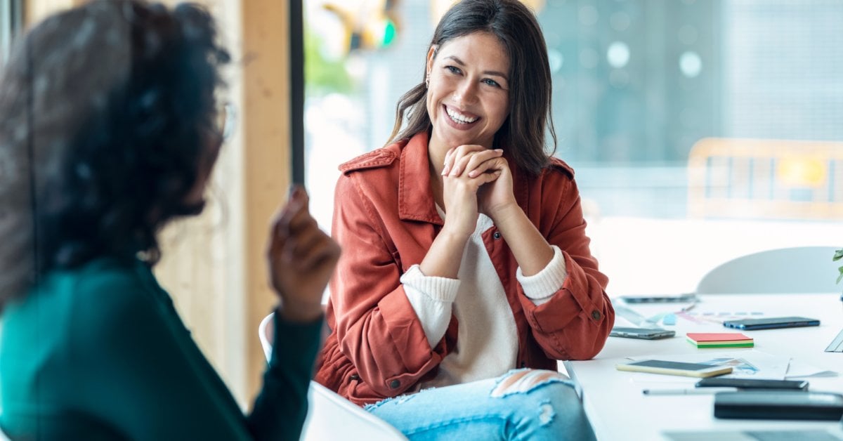 Two women sit across from each other in a bright office, smiling and engaged in an open, positive conversation.