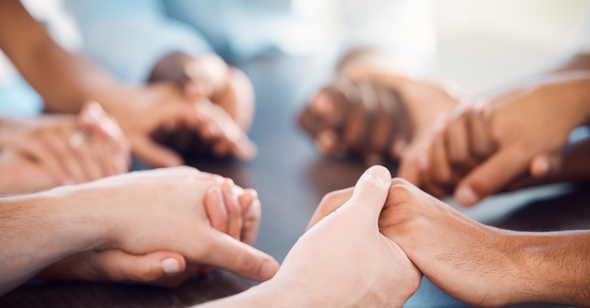 A diverse group of people holding hands around a table, symbolizing community support and connection.
