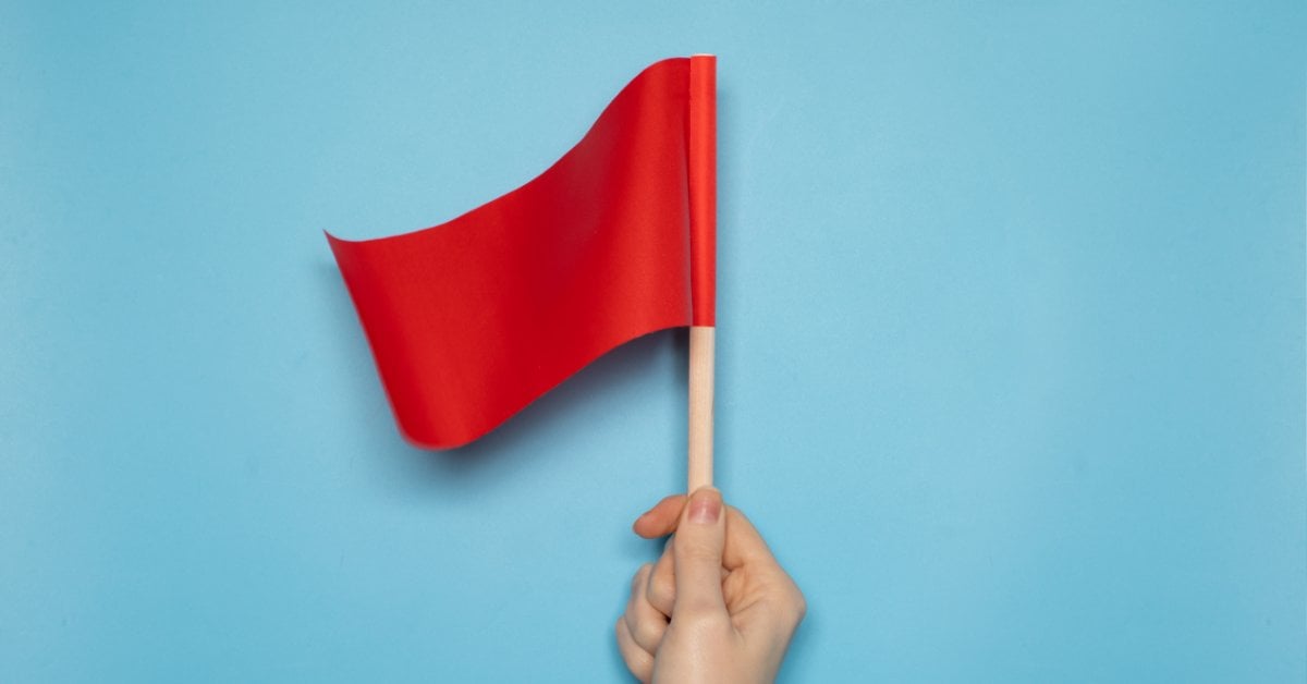 A hand holds a small red flag against a light blue background, symbolizing warning signs in mental health treatment.