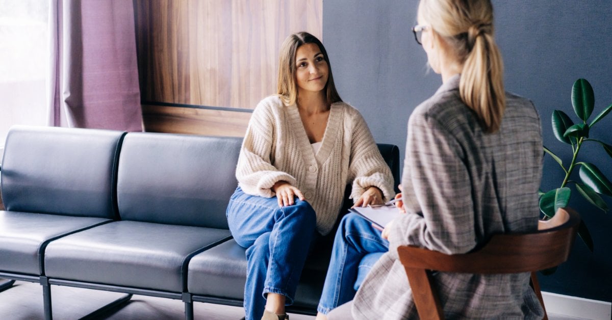 A young woman sits across from her therapist during an in-person talk therapy session in a calm office setting.