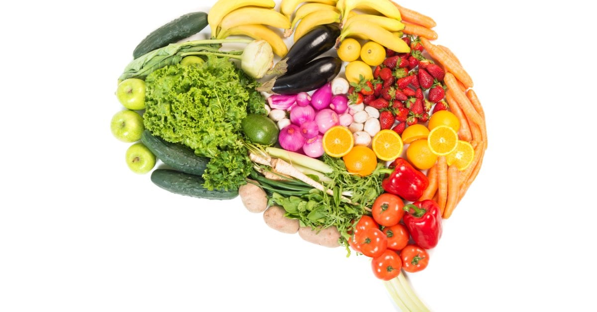 Colorful fruits and veggies are arranged in the shape of a human brain. They include bananas, leafy greens, and carrots.
