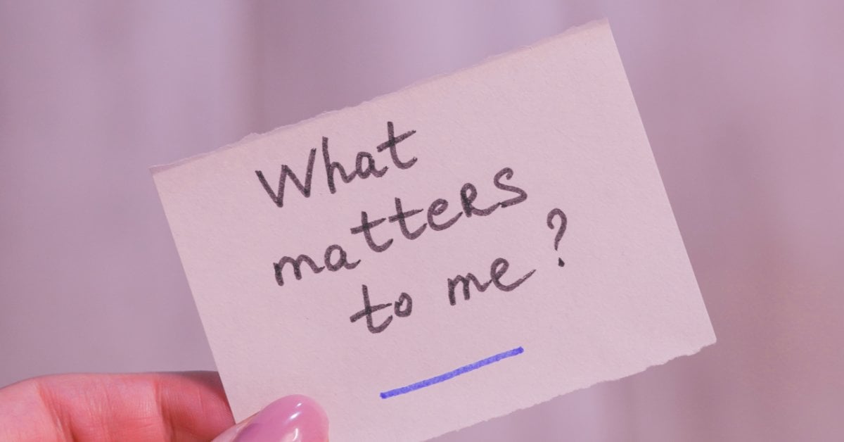 A hand holds a piece of paper with the handwritten words “What matters to me?” A blue line is beneath the question.