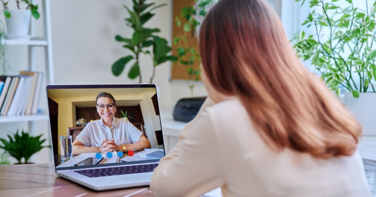A person participates in a video call using a laptop. A smiling woman wearing glasses is visible on the screen.