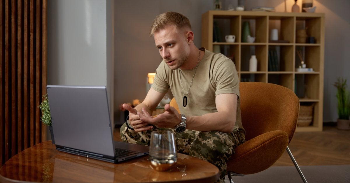 Man wearing military dog tags speaking during a video call, discussing his mental health from home.
