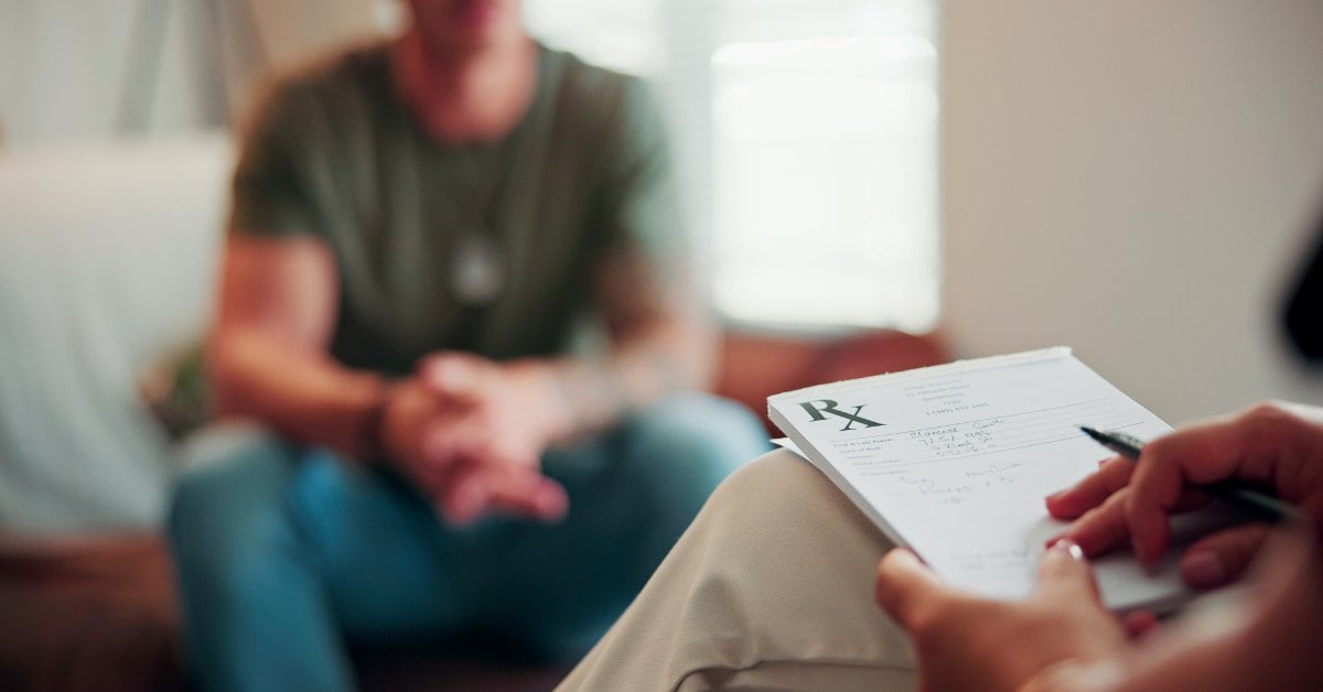 Provider writing on a prescription pad while a patient sits nearby during a psychiatric appointment.